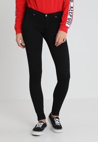 Jeans ajustados de mezclilla negra con una textura suave, que cuentan con una cintura de altura media, dos bolsillos frontales y cierre de botón metálico y cremallera.