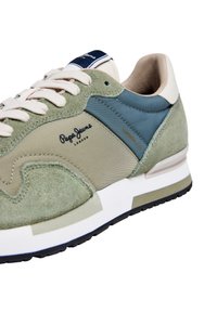 Baskets vertes et bleues en daim et tissu, forme amande, semelle blanche et logo sur le côté. Présentent des accents beiges.