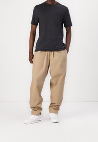 Tmavě šedé tričko z bavlny s krátkým rukávem spojené s béžovými kapsáčovými kalhotami s dvěma velkými kapsami a bílými teniskami s šedými detaily.