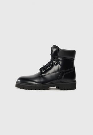 Bottine en cuir noir avec une finition brillante, design à lacets, col rembourré et semelle en caoutchouc robuste avec des grips de traction.