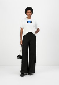 Witte T-shirt met blauw hartgrafiek, gecombineerd met hoge zwarte wijde broek met zijzakken en een kleine zwarte handtas.