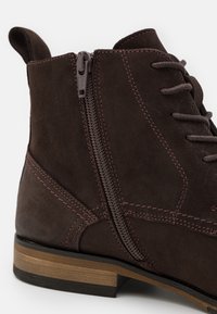 Bottine en daim marron à finition texturée, équipée d'une fermeture éclair latérale, de coutures marron et d'un talon en bois empilé.