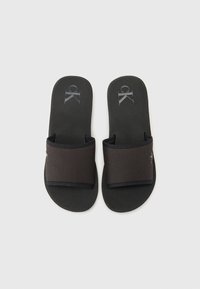 Sandale negre tip slide cu talpă interioară căptușită și o curea lată din țesătură cu un logo. Suprafață texturată cu un finisaj mat și neted.