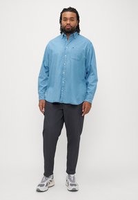 Jasnoniebieska koszula z denimu na guziki z długimi rękawami, kieszenią na piersi, w parze z ciemnoszarymi spodniami i szarymi butami sportowymi. Prosty krój, casualowy fason.