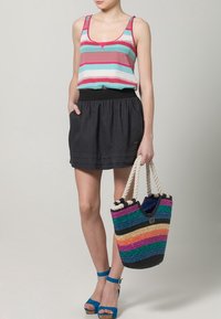 Camiseta sin mangas a rayas en rosa y turquesa, falda negra hasta la cintura, sandalias azules y un bolso colorido tejido con asas de cuerda.