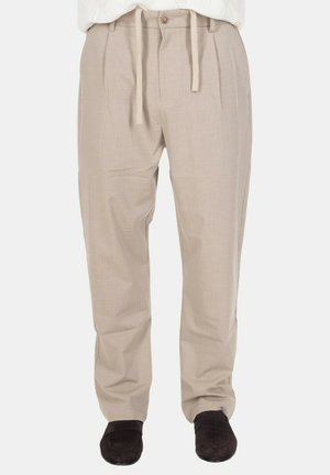 Pantaloni beige a gamba dritta con vita con bottone e coulisse, indossati con scarpe marrone scuro senza lacci.