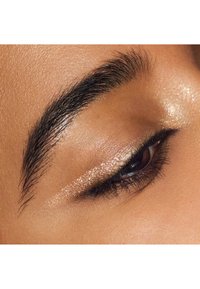 Primer plano de un ojo con pestañas oscuras; párpado resaltado con sombra de ojos en un tono rosa dorado brillante, textura de piel suave y ceja bien cuidada.