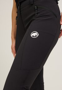 Svarta träningsbyxor med en åtsittande design, utrustad med en ficka med dragkedja och en vit logotyp av en elefant på låret. Slät textur.