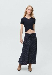 Črn rebrast crop top z V-izrezom, v kombinaciji z dolgim mornarsko modrim krilom z diskretnim cvetličnim vzorcem in vrvico za prilagajanje.