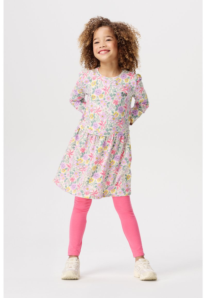 Robe à motifs floraux dans des teintes de rose, vert et blanc, avec une jupe froncée et des manches longues, associée à des leggings rose vif et des baskets.
