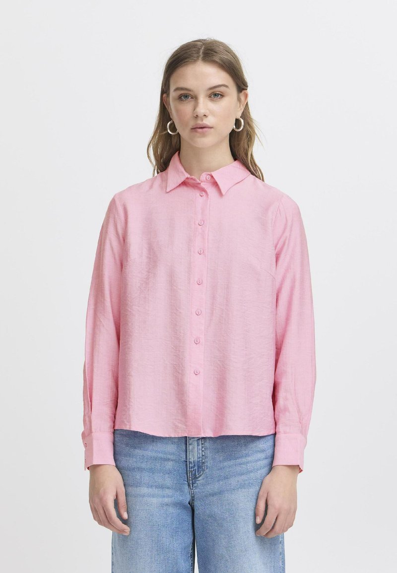Rosa langärmliges Hemd mit durchgehender Knopfleiste, Kragen und lockerer Passform, aus strukturiertem Stoff; kombiniert mit hellblauen Jeans.