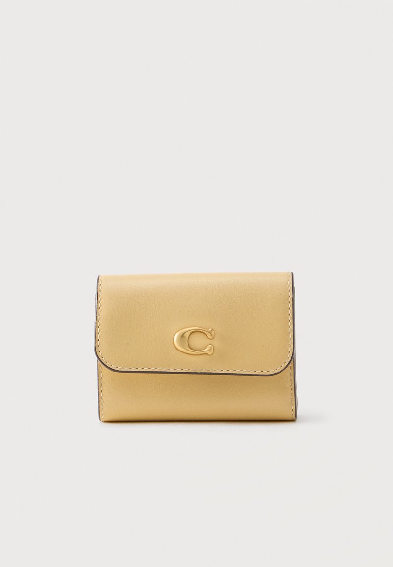 Συμπαγές μπεζ δερμάτινο πορτοφόλι με στρογγυλεστό καπάκι και χρυσόλογο έμβλημα "C" στο κέντρο του μπροστινού μέρους σε απλό φόντο.