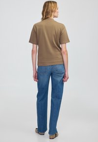 Bruine, korte mouwen t-shirt met een ontspannen pasvorm, gecombineerd met blauwe denim jeans. Het bovenstuk heeft een ronde hals en een gladde textuur.