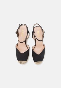 Zapatos de tacón slingback de tela negra con un frente en forma de V, detalles de crochet beige en la punta y una correa ajustable. Nombre de la marca grabado en el interior.