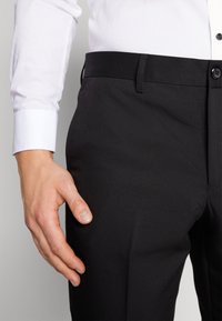 Black trousers made of smooth fabric with a straight design. Features a subtle texture, side pockets, and a button closure at the waist.