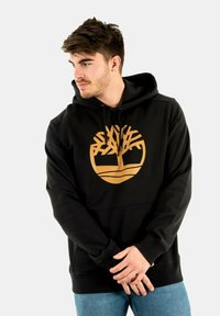 Zwarte hoodie van zachte stof met een groot gouden boomlogo. Het heeft een kangoeroezak en een capuchon met trekkoord. Casual pasvorm, ribgebreide mouwboorden.