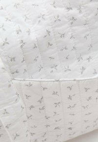 Quilted blanket in white fabric with gray leaf motifs. Features stitched patterns and a smooth texture, designed for warmth and comfort.