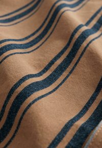 Baumwollstoff mit wellenförmigen marineblauen Streifen auf beigem Hintergrund, verfügt über eine glatte Textur und sichtbare Nähte entlang der Kanten.