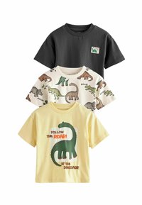 Tři trička na sobě. Černé bavlněné s logem, krémové bavlněné s dinosaurími vzory a žluté bavlněné s grafikou zeleného dinosaura.