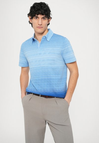 Polokošeľa s krátkym rukávom v modrom gradiente s horizontálnymi pruhmi, s golierom a ľahkou textúrou, v kombinácii s béžovými nohavicami.