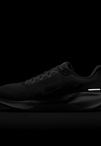 Chaussure de running basse noire avec dessus en mesh, design à lacets, logo Nike sur le côté et semelle texturée sur fond sombre.