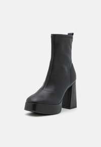Sorte ankelboots i sort lær med en kraftig blok hæl og sømløs design, med en pull tab for nem påtagning.