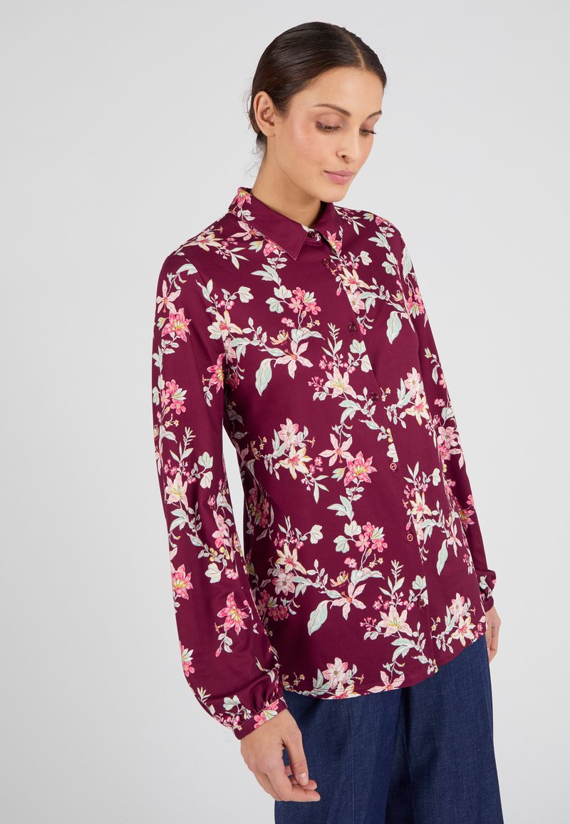Blusa floral burdeos de manga larga, con botones en la parte delantera, que presenta patrones de flores en rosa y verde sobre una tela suave.