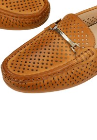 Mocassins en cuir marron clair avec un design perforé et un détail en barre métallique sur le dessus.