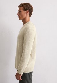 Beige Strickpullover mit V-Ausschnitt, gerippten Bündchen und Saum. Der strukturierte Stoff hat ein weiches Aussehen und betont einen lässigen Stil.