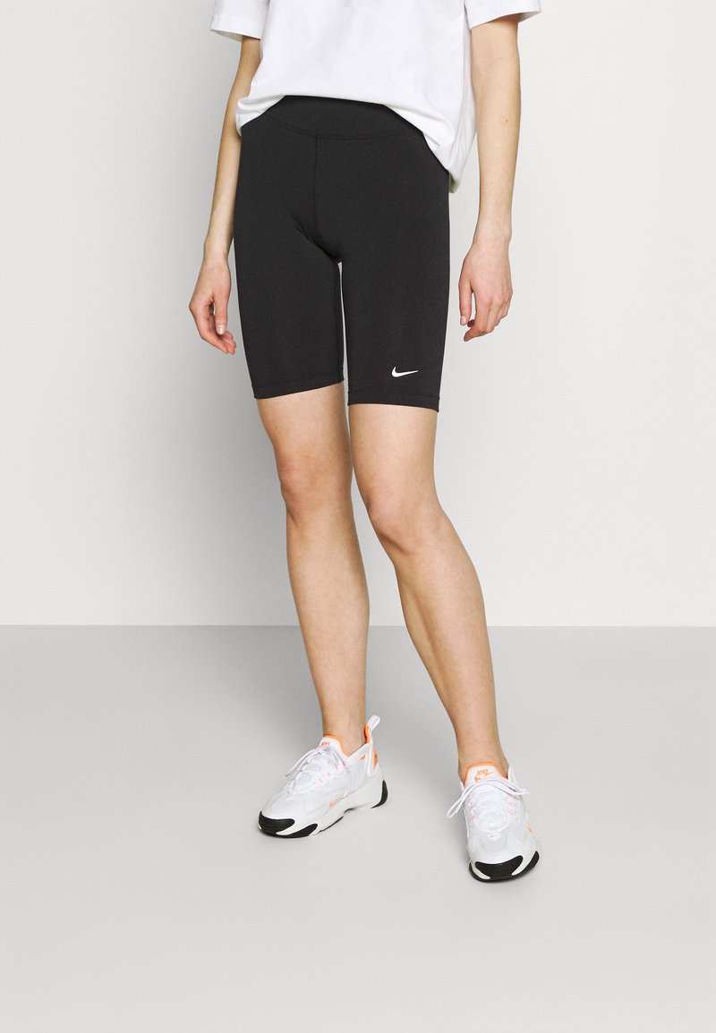 Svarta cykelshorts i elastiskt tyg, med en bred midja och en liten vit Nike-logga på låret. Bärs med vita träningsskor.