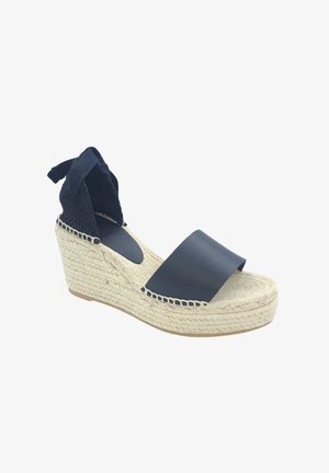 Espadrilles de cuña en azul marino con una tira de cuero suave en la puntera y lazos de tela trenzada en el tobillo. La suela de plataforma envuelta en yute aporta textura.