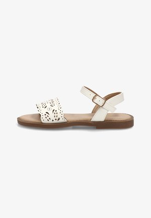 Sandalia plana blanca con tira frontal floral cortada con láser, tira ajustable en el tobillo con hebilla dorada y suela acolchada marrón.