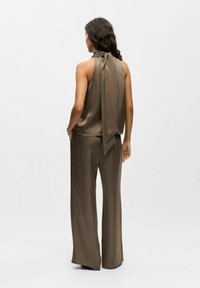 Satin ärmelloses Oberteil mit einer geknoteten Rückendetail, kombiniert mit weiten Hosen, beide in einem gedämpften Olivgrün. Glatte Textur, fließendes Design.