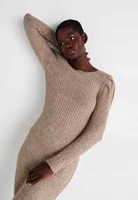 Abito a coste beige con maniche lunghe e scollatura a girocollo, caratterizzato da dettagli delle cuciture sottili e una silhouette aderente.