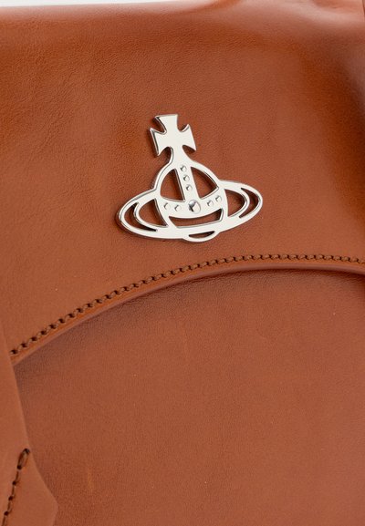 Smeđa kožna torba s metalik logotipom koji prikazuje križ i kružne elemente. Glatka tekstura s vidljivim detaljima šivanja.