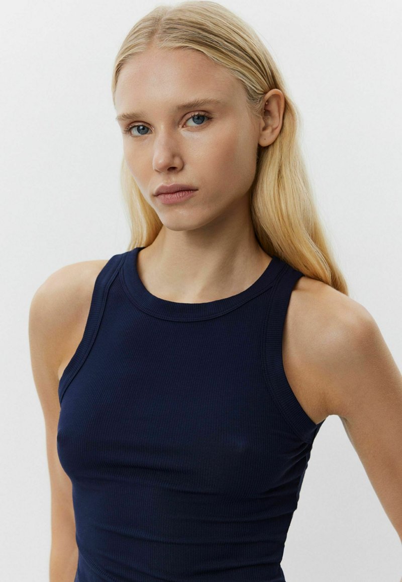 Tengerészkék bordázott ujjatlan top, kerek nyakkivágással. Anyaga sima tapintású és testhez simuló fazonú, mely kiemeli a test kontúrjait.