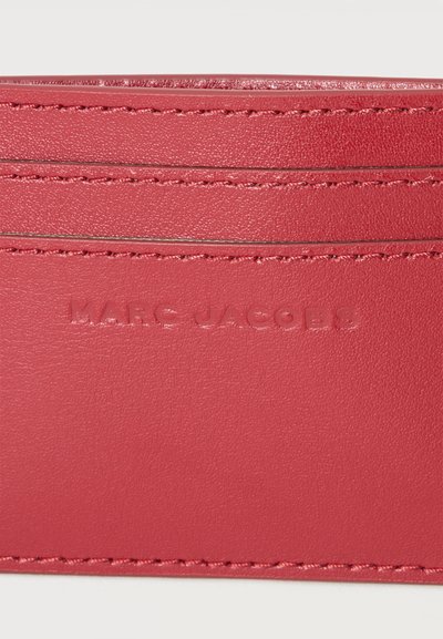 Porte-cartes en cuir rouge avec logo "MARC JACOBS" embossé et coutures visibles le long des bords.
