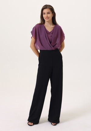 Top de gasa morado con un diseño drapeado sobre un mono negro de pierna ancha. El top presenta un escote en V con lentejuelas. Tacones abiertos negros.
