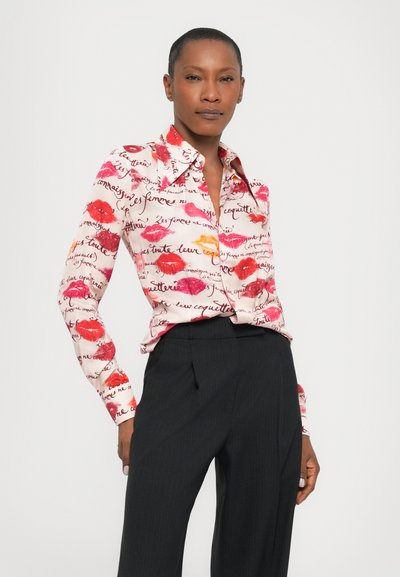 Button-down shirt in lightweight fabric, featuring a pink and red lip print with text; paired with tailored dark trousers for contrast.