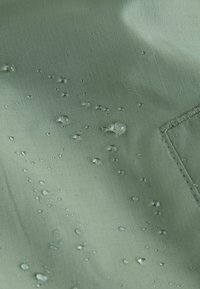 Water droplets beading on light green waterproof fabric with visible stitching on the right side.