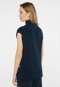 Marineblaues, ärmelloses Stricktop mit hohem Kragen, strukturiertem Stoff und seitlichen Schlitzen. Schlichtes Design ohne sichtbare Beschläge oder Akzente.