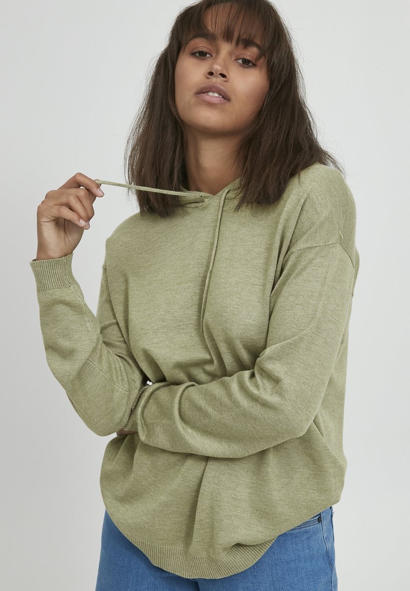 Sudadera verde claro hecha de material suave, con capucha ajustable, puños acanalados y un ajuste relajado. Combinada con jeans azules.