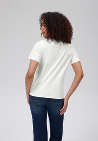 Hvit T-skjorte med korte ermer og rund hals, kombinert med mørkeblå denimjeans. Glatt stoff og tilpasset design.
