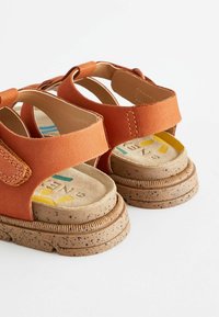 Oranga sandaletter med en mocka finish, försedd med ett kardborreband och en brunprickig gummisula. Fotränna med vaddering och färgglad varumärkesdetalj.