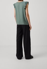 Haut vert texturé avec des détails de manches froncées, associé à un pantalon noir ample. La tenue présente un design décontracté et relax.