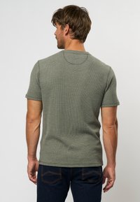 Tricou scurt cu mânecă scurtă de culoare verde măslinie, dintr-un material texturat, cu decolteu rotund și siluetă ajustată, asortat cu blugi de denim închis.