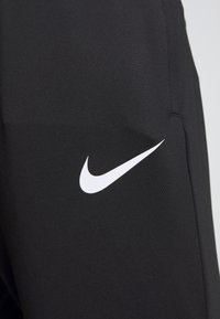Närbild av svart tyg med vit Nike swoosh-logotyp på kläder, som visar textur och sömdetaljer.