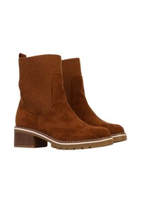 Bruine nubuck enkellaarsjes met ribstof aan de bovenkant, ronde neus en een blokhak van 5 cm. Voorzien van een rubberen zool en witte stikselaccenten.