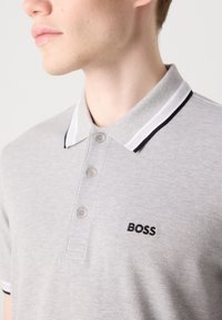 Γκρι πόλο μπλουζάκι με υφή, τρία κουμπιά και γιακά με λευκές και μαύρες ρίγες. Διαθέτει το μαύρο λογότυπο "BOSS".