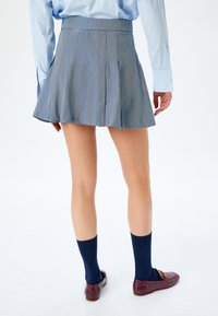 Falda azul plisada de tela texturada, de longitud media, combinada con calcetines azul oscuro y mocasines burdeos, que muestra un diseño a medida.